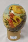 A hand-decorated blown ostrich egg, nicely painted with feeding chicks within a nest, signed '