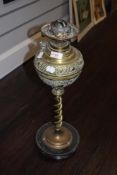 A late 19th century embossed brass oil lamp, having twist stem and wooden base, void of chimney.