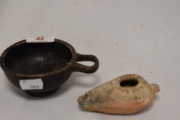 An earthenware oil lamp, measuring 10cm long, & a Greek style ebonised cup with ring handle