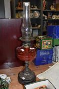 A late 19th Century oil lamp, having a cranberry glass reservoir and a pierced cast metal base,