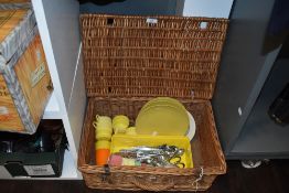 A vintage wicker picnic basket containing Melaware plates, cutlery, and beakers