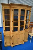 A modern stained pine effect breakfront bookcase with panelled base section