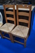 A pair of vintage beech ladder back kitchen chairs having rush seats