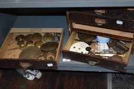 A box of brass pendulum bobs and another containing clock faces and workings