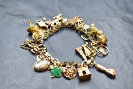 A yellow metal charm bracelet having 23 charms, many stamped 375 including harp, cactus, bagpipes