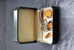 Three pieces of amber style jewellery having carved floral decoration in white metal mounts, no