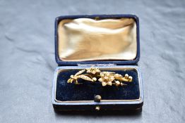 A yellow metal brooch stamped 18 in the form of a tied sprig of flowers with seed pearl and