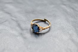 A yellow metal ring having oval blue paste stone in a four claw mount to open shoulders on a split