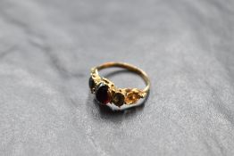 A garnet cabochon ring flanked by two paste stones, all in an ornate mount with filled backs on a