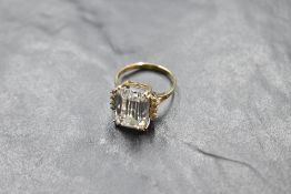 A large baguette cut cubic zirconia ring having further stones to shoulders on a split 14ct gold