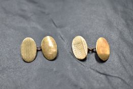 A pair of 9ct gold cufflinks of oval form having chain connectors and engine turned decoration,