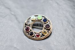 A white metal brooch of open circular form set with nine stones, including opal, garnet, citrine,