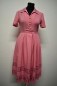 A 1950s candy pink linen day dress, having embroidery to collar, reverse of bodice and hem in blue