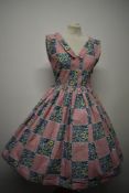A 1950s cotton day dress, having floral pattern interspersed with squares of cross motif design,