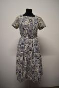 A 1950s bark cloth day dress in white, having navy blue geometric pattern, side zip and pleated