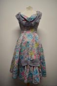 An unusual 1950s day dress, having abstract floral print with contrasting lilac ribbon detailing,