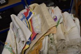 A box full of vintage table linen, including embroidered table cloths and other colourful examples.
