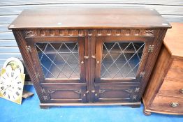 A dark stained Priory style low bookcase having leaded glass doors and lower cupboard section