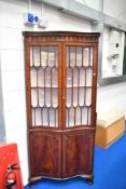 A 1920s mahogany serpentine fronted corner display cabinet with cupboard under