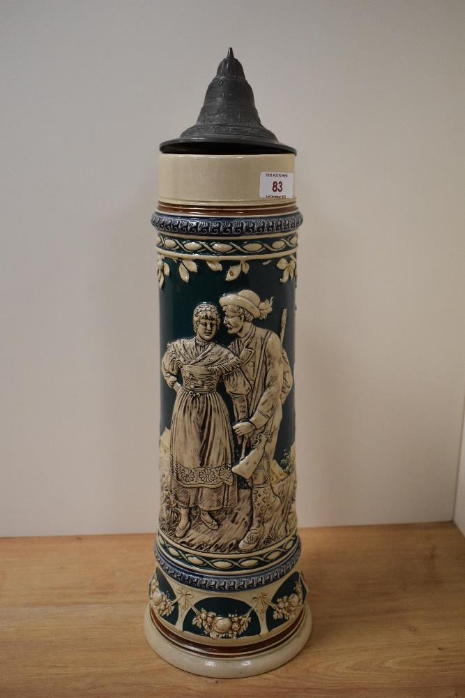 An oversized Stein, having metal lid and design depicting couple and swags with fruit.