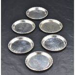 A group of six small white metal coasters, of slightly dished circular form with moulded egg-and-