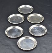 A group of six small white metal coasters, of slightly dished circular form with moulded egg-and-