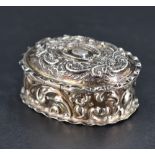 A small Edwardian silver box, of hinged oval form embossed with foliate and scroll decoration, marks
