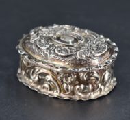 A small Edwardian silver box, of hinged oval form embossed with foliate and scroll decoration, marks