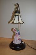 A continental porcelain figural table lamp, with a Tiffany style glass shade, measuring 51cm
