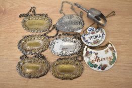 A collection of silver tone and enamel decanter labels, also included is a bottle stop.