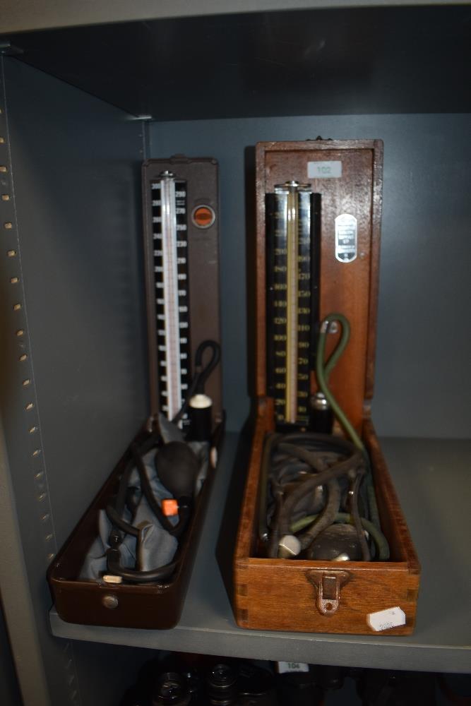 Two early to mid 20th Century sphygmomanometers, blood pressure monitors, one housed within a
