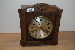 An early 20th Century oak cased mantel clock, the shaped pediment above a silvered Roman dial,