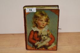 A vintage tin money box in the form of a book with depiction of child and dog to front, with key.