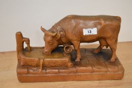A carved wooden cow, depicted drinking from trough.