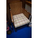An early 20th Century mahogany framed easy armchair having canework panels and later tweed