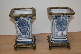 Two blue and white vases, having foliate transfer decoration sat on moulded brass base, and edged in