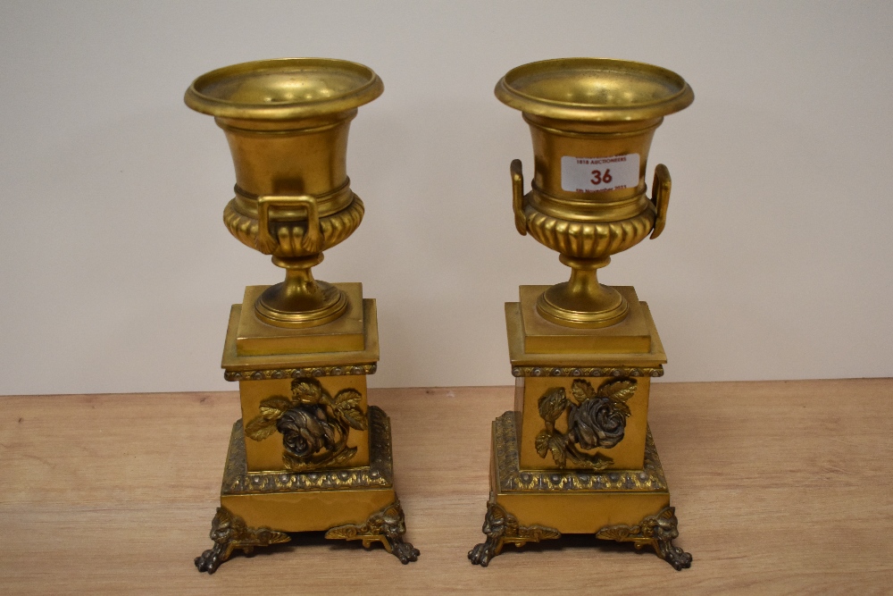 Two ormolu clock garnitures, of campana urn form, both having rose decoration, clawed feet with lion