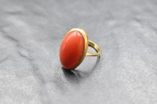An oval coral cabochon set ring in a collared mount on a yellow metal loop stamped 750, size L &