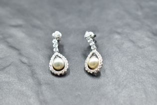 A pair of 18ct white gold diamond stud earrings having collared diamond drops to swing pearls in a