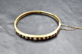 A hinged gold bangle having diamond and split pearl decoration to front panel, no marks but presumed