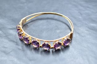 A yellow metal hinged bangle stamped 14 of open tubular form having seven inset amethysts, approx