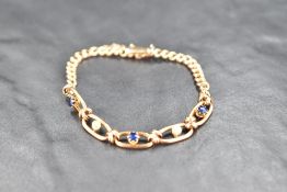 A rose gold bracelet having five open panels set with seed pearls and sapphires on a curb chain with
