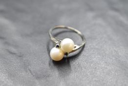 A cultured pearl crossover ring with sapphire chip set shoulders on a white metal loop stamped