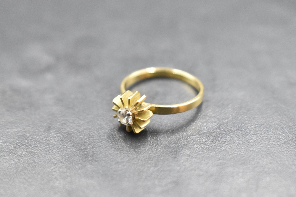 A diamond solitaire ring, approx 0.125ct in a 4 claw set stylised sun buerst mount on an 18ct gold