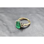 A diamond and baguette cut green stone trilogy ring, central stone probably an emerald as bearing