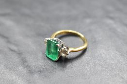 A diamond and baguette cut green stone trilogy ring, central stone probably an emerald as bearing