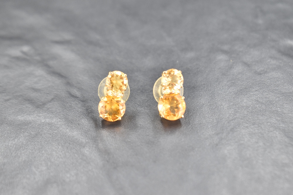 A pair of double stone citrine stud earrings spaced by a row of diamond chips, all in a yellow metal