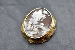 A conch shell cameo brooch bearing a countryside scene in an engraved yellow metal mount with hair