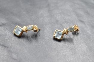 A pair of 9ct gold earrings having baguette cut collared aquamarine studs with gold drops to further