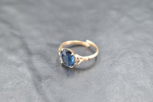 A yellow metal ring having oval blue paste stone in a four claw mount to open shoulders on a split